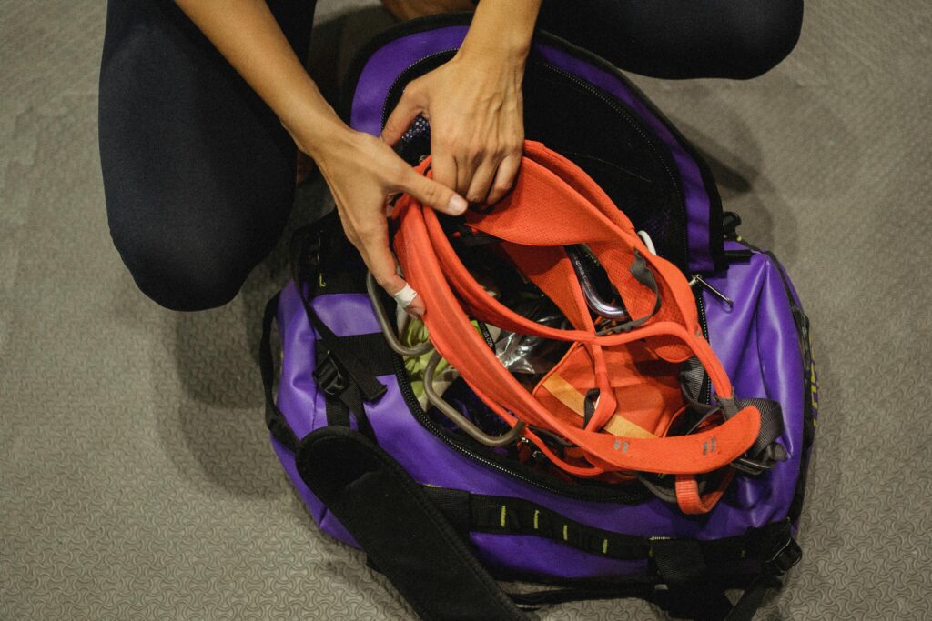 Hands packing climbing harness into purple sports bag, indoors.